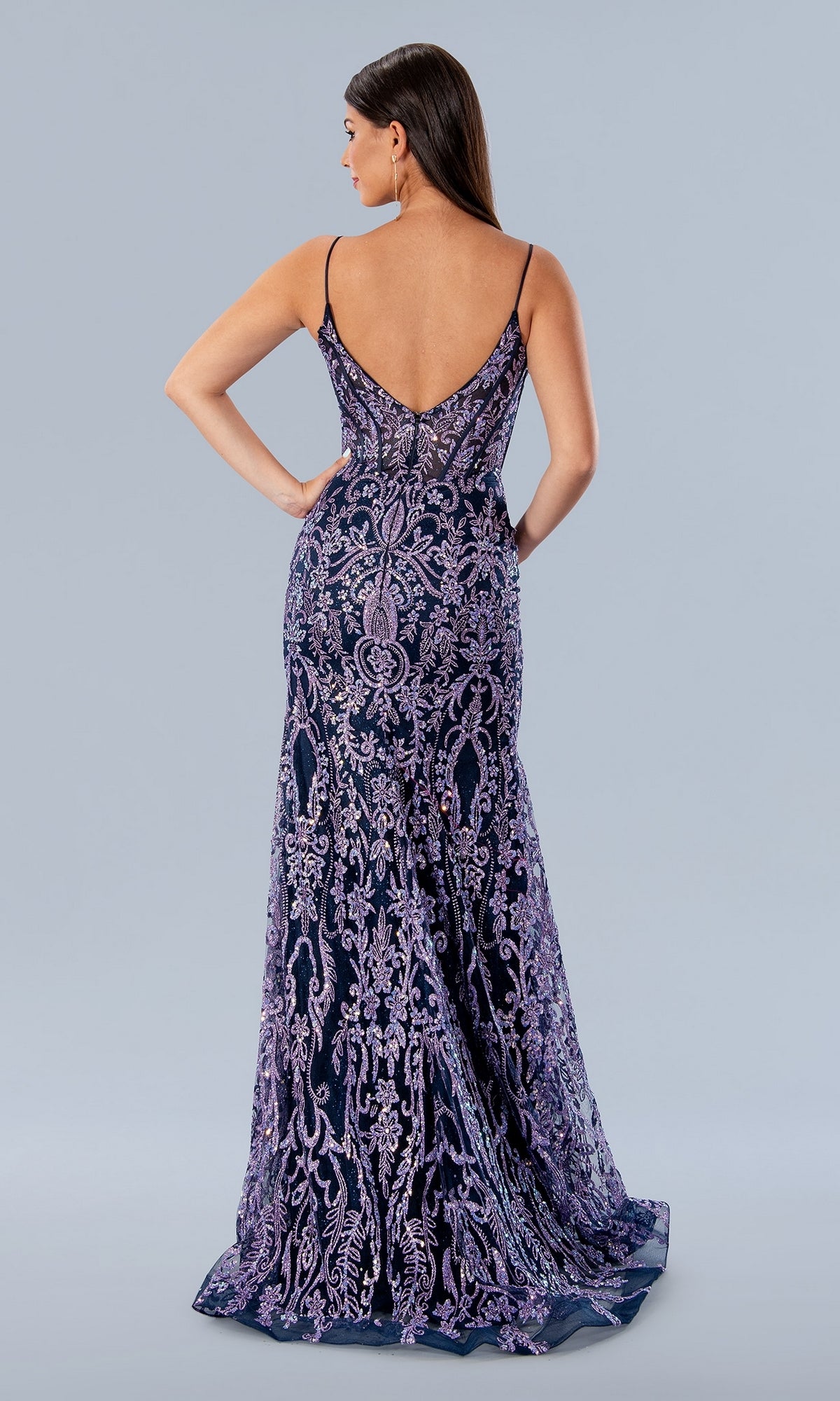 A woman poses against a light gray background wearing the Long Prom Dress 24168 by Stella Couture, a fitted, floor-length purple lace evening gown with thin straps, low v-neckline, and open back.
